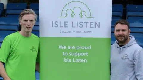 ISLE LISTEN Sean Quaye of FC Isle of Man and Adam Hudgeon of Isle Listen standing next to a banner