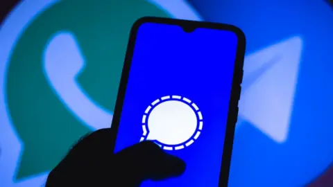Getty Images A person holds a phone with Signal's logo on it, in front of a WhatsApp logo