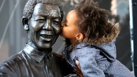 Getty Images A young South African girl names Malika is lifted by her mother to kiss a statue of former South African President Nelson Mandela before a service conducted by Archbishop Desmond Tutu at the Nelson Mandela Foundation on December 9, 2013 in Johannesburg, South Africa