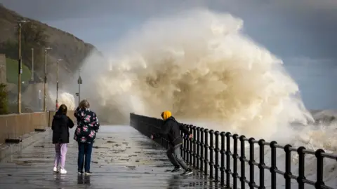 Getty Images People walking in Folkestone while waves created by Storm Ciarán crash into the promenade