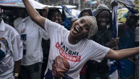 AFP Supporters of the incumbent president President Felix Tshisekedi gesture in the rain prior to his arrival for a campaign rally in Goma, capital of North Kivu province, eastern Democratic Republic of Congo, on December 10, 2023.