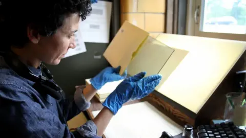 Alex Newman/PRI Curatorial assistant Anne Callahan inspects a plate before it is cleaned for scanning. She makes sure the metadata from the paper jacket is properly entered into the computer before the plate goes to be wiped down and then scanned.