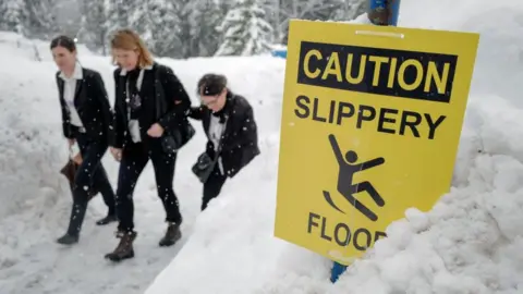 Getty Images Staff members walk under snowfall next to the Congress Centre ahead of the World Economic Forum (WEF) 2018 annual meeting, on January 22, 2018 in Davos