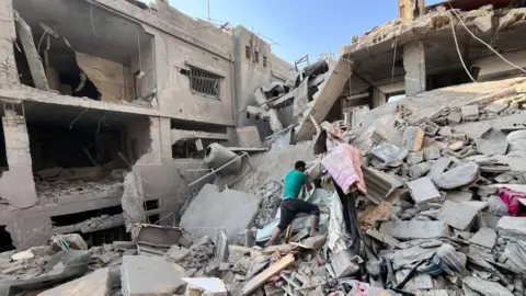AFP A Palestinian man searches for missing family members under the rubble of a building destroyed by an Israeli strike, in Beit Lahia, in the northern Gaza Strip (7 November 2024)