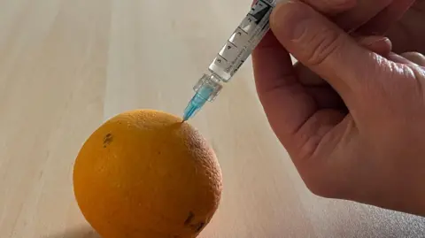 Julia Gregory/BBC Someone injecting a orange using syringe
