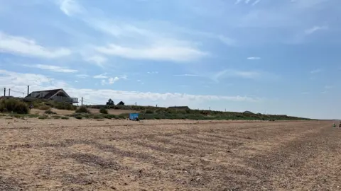 BBC Bright blue sky above sand dunes peppered with mahram grass and a shingle beach at Heacham in Norfolk