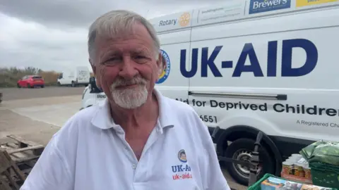 John Fairhall/BBC Alan Hilliar in front of a UK-Aid van.