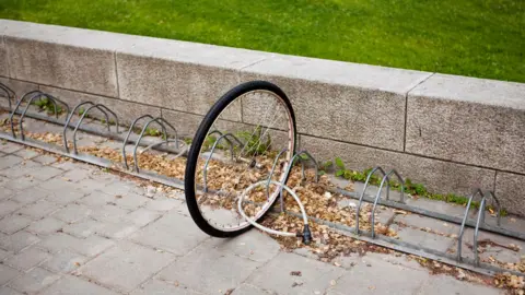 Getty Images A bicycle wheel sits locked to a rail. The rest of the bike is seemingly missing.