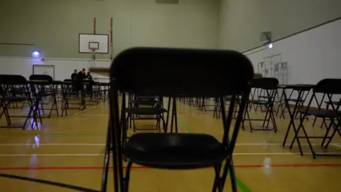 BBC News A sports hall, with tables and chairs set up for an exam