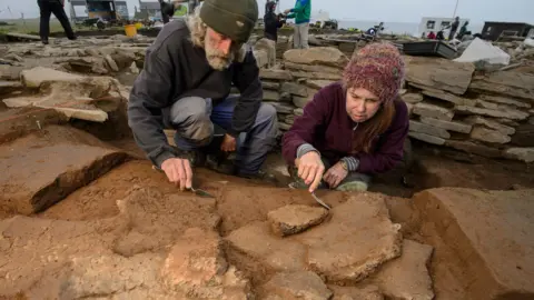 Jim Richardson Two archaeologists working with trowels on stones at the dig
