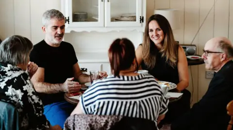 Rod Dodsworth Dr Verena Niyadurupola (right) in a coaching session, with four other people, smiling at them, all sat round a small round table
