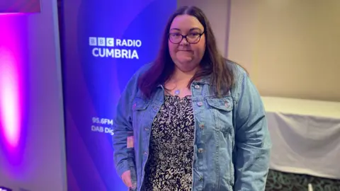 Ally standing in front of a BBC Radio Cumbria sign.