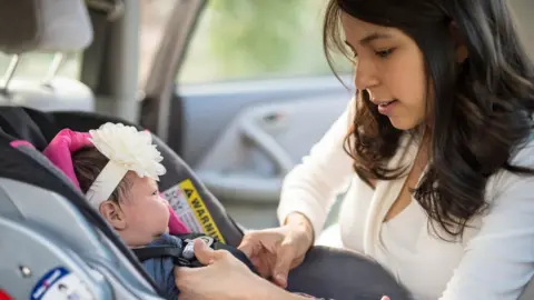 Getty Images Mother secures her child in its car seat