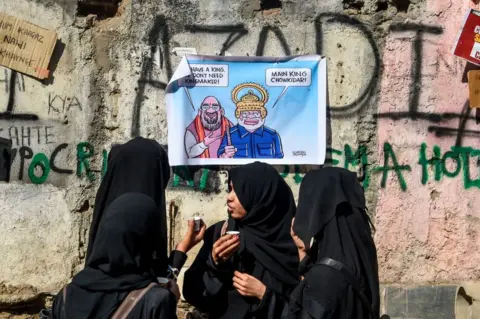 Getty Images Muslim women drink chai (tea) on a street in front of a wall covered with posters and graffitis to protest against India's new citizenship law, during a demonstration in Mumbai on January 30, 2020.