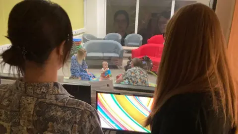 BBC Baby plays with toys while watched by scientists through a screen