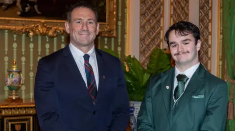DofE/Jonny Sanders Jason Fox, standing next to Harry Jones, both men are looking straight at the camera and smiling. Jason (left) is wearing a blue suit