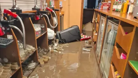 Blackwood Rugby Club A flooded bar is seen with a few centimetres of water visible. A bin is on its side with several items scattered floating in the water.