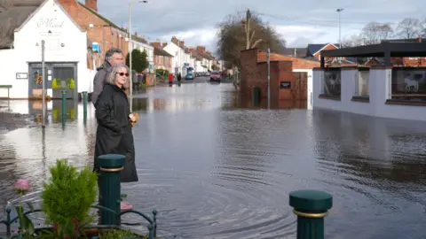 PA Media A man and woman stood in floodwater in the village of Quorn, Leicestershire.