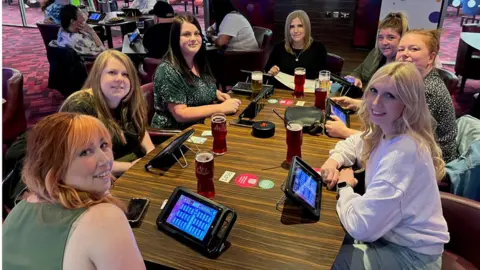 BBC Becki Tate and six friends around a table playing bingo on tablet devices